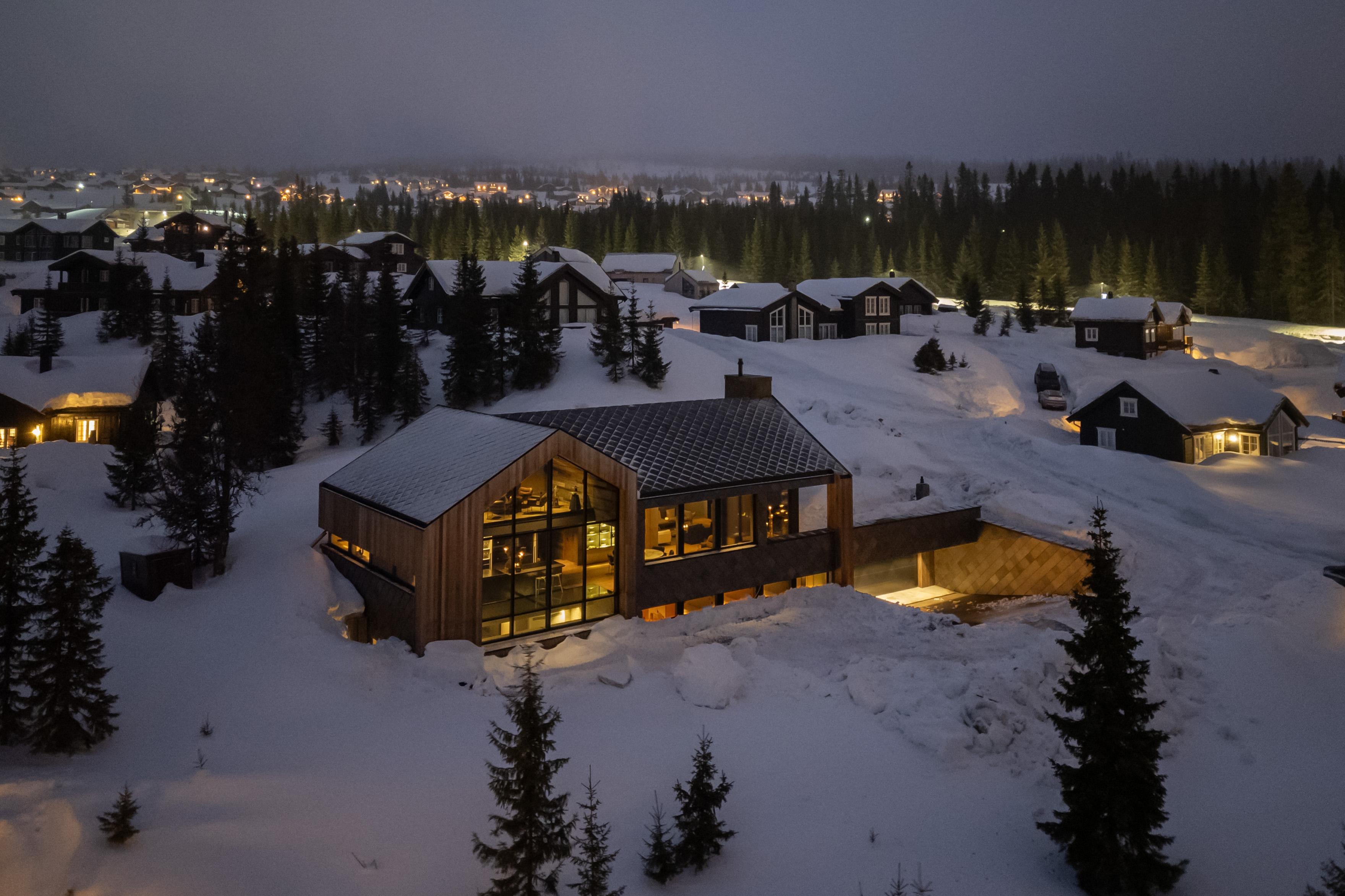 Nye hytter i snøen i skumringen, med lys i vinduene